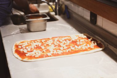 Pizza şefi ticari bir mutfakta sosu tabana koydu.