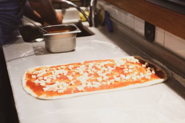 Pizza şefi ticari bir mutfakta sosu tabana koydu.