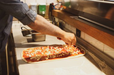 Pizza şefi ticari bir mutfakta sosu tabana koydu.