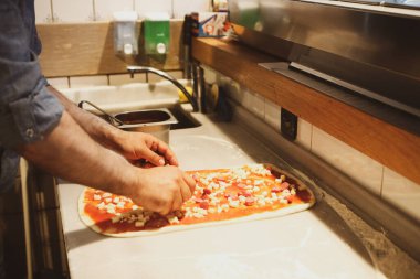 Pizza şefi ticari bir mutfakta sosu tabana koydu.