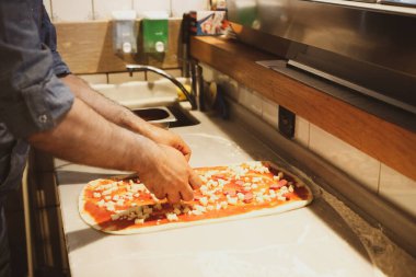Pizza şefi ticari bir mutfakta sosu tabana koydu.