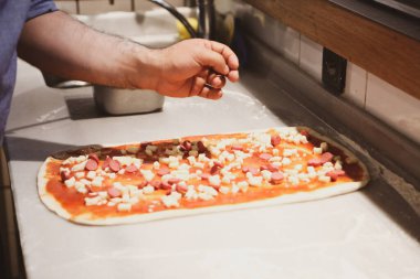 Pizza şefi ticari bir mutfakta sosu tabana koydu.