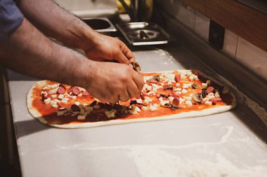 Pizza şefi ticari bir mutfakta sosu tabana koydu.