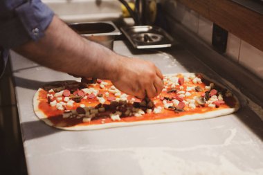 Pizza şefi ticari bir mutfakta sosu tabana koydu.