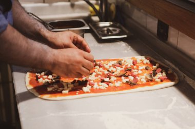 Pizza şefi ticari bir mutfakta sosu tabana koydu.