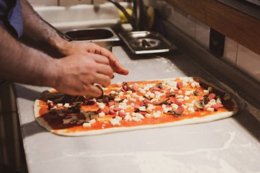 Pizza şefi ticari bir mutfakta sosu tabana koydu.