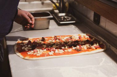 Pizza şefi ticari bir mutfakta sosu tabana koydu.