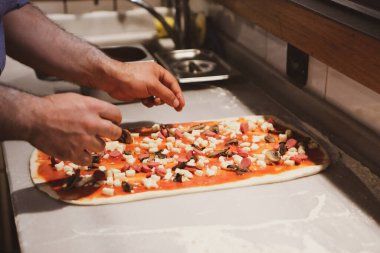 Pizza şefi ticari bir mutfakta sosu tabana koydu.