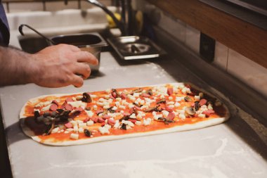 Pizza şefi ticari bir mutfakta sosu tabana koydu.