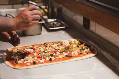 Pizza şefi ticari bir mutfakta sosu tabana koydu.