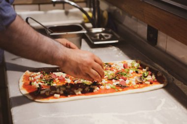 Pizza şefi ticari bir mutfakta sosu tabana koydu.