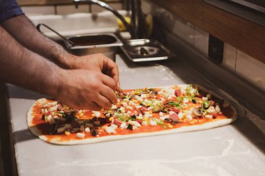 Pizza şefi ticari bir mutfakta sosu tabana koydu.