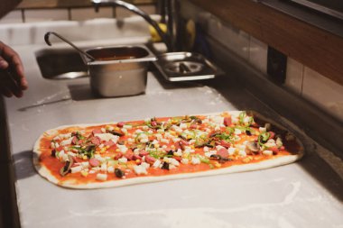 Pizza şefi ticari bir mutfakta sosu tabana koydu.