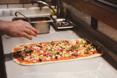 Pizza şefi ticari bir mutfakta sosu tabana koydu.