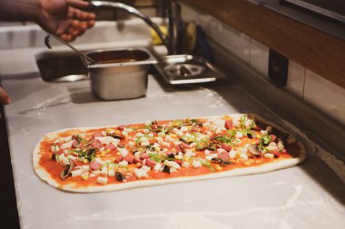 Pizza şefi ticari bir mutfakta sosu tabana koydu.