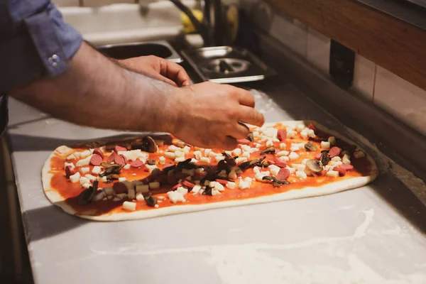 Pizza şefi ticari bir mutfakta sosu tabana koydu.