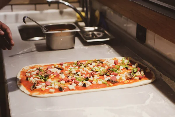 Pizza şefi ticari bir mutfakta sosu tabana koydu.