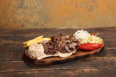 Doner kebabı kesme tahtasının üzerinde duruyor. Et, soğan ve salata ile Shawarma eski ve karanlık bir tahta masada yatıyor.
