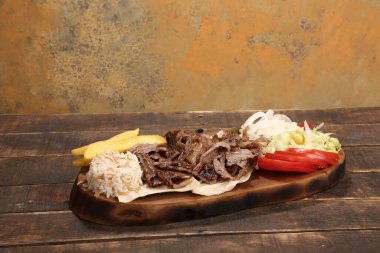 Doner kebabı kesme tahtasının üzerinde duruyor. Et, soğan ve salata ile Shawarma eski ve karanlık bir tahta masada yatıyor.