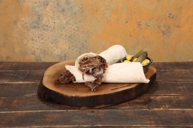 Doner kebabı kesme tahtasının üzerinde duruyor. Et, soğan ve salata ile Shawarma eski ve karanlık bir tahta masada yatıyor.