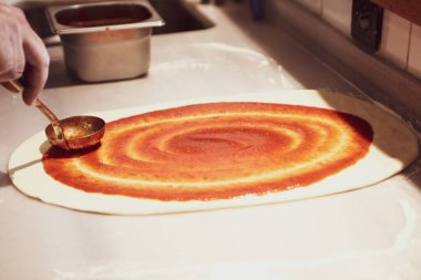 Pizza şefi ticari bir mutfakta sosu tabana koydu.
