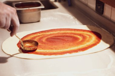 Pizza şefi ticari bir mutfakta sosu tabana koydu.