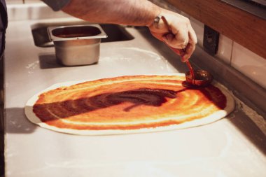 Pizza şefi ticari bir mutfakta sosu tabana koydu.