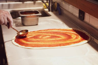 Pizza şefi ticari bir mutfakta sosu tabana koydu.
