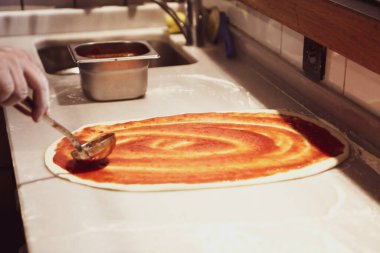 Pizza şefi ticari bir mutfakta sosu tabana koydu.