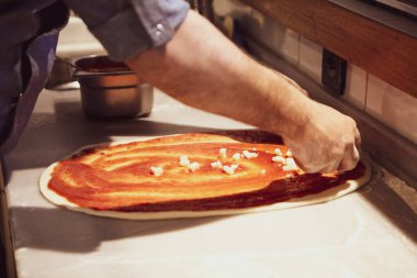 Pizza şefi ticari bir mutfakta sosu tabana koydu.