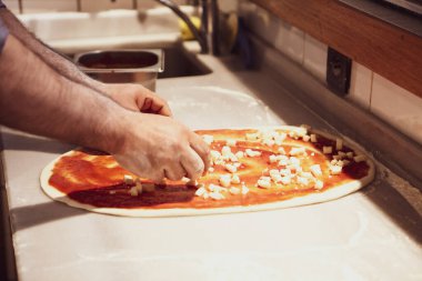 Pizza şefi ticari bir mutfakta sosu tabana koydu.