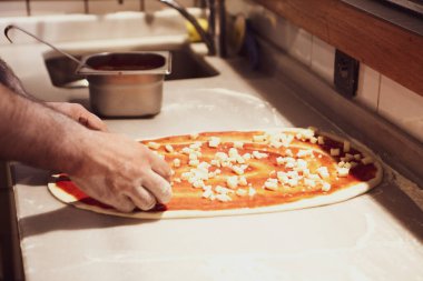 Pizza şefi ticari bir mutfakta sosu tabana koydu.