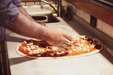 Pizza şefi ticari bir mutfakta sosu tabana koydu.
