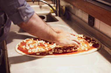 Pizza şefi ticari bir mutfakta sosu tabana koydu.