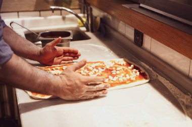 Pizza şefi ticari bir mutfakta sosu tabana koydu.