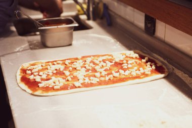 Pizza şefi ticari bir mutfakta sosu tabana koydu.