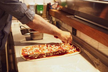 Pizza şefi ticari bir mutfakta sosu tabana koydu.