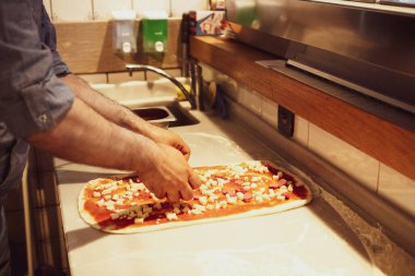Pizza şefi ticari bir mutfakta sosu tabana koydu.