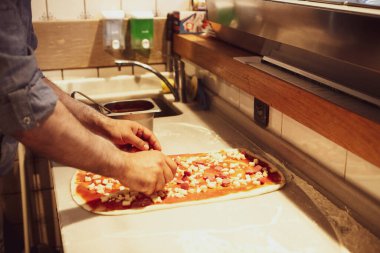 Pizza şefi ticari bir mutfakta sosu tabana koydu.