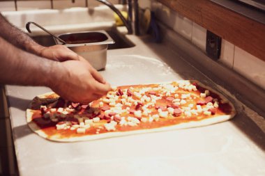 Pizza şefi ticari bir mutfakta sosu tabana koydu.