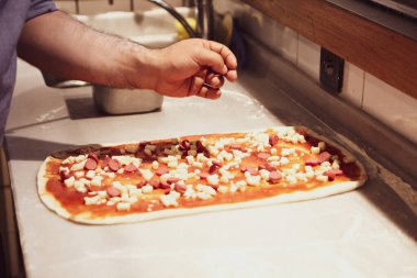 Pizza şefi ticari bir mutfakta sosu tabana koydu.