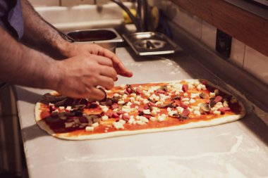 Pizza şefi ticari bir mutfakta sosu tabana koydu.