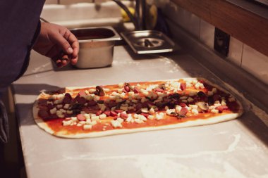 Pizza şefi ticari bir mutfakta sosu tabana koydu.