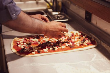 Pizza şefi ticari bir mutfakta sosu tabana koydu.