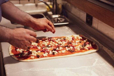 Pizza şefi ticari bir mutfakta sosu tabana koydu.