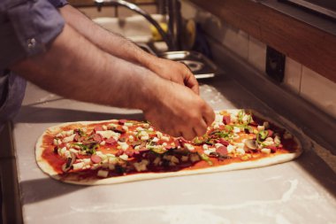 Pizza şefi ticari bir mutfakta sosu tabana koydu.