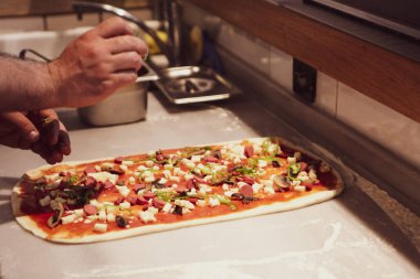 Pizza şefi ticari bir mutfakta sosu tabana koydu.