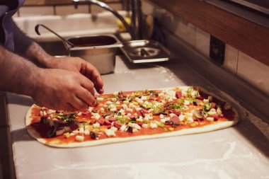 Pizza şefi ticari bir mutfakta sosu tabana koydu.