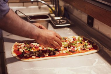 Pizza şefi ticari bir mutfakta sosu tabana koydu.