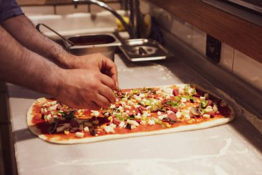 Pizza şefi ticari bir mutfakta sosu tabana koydu.